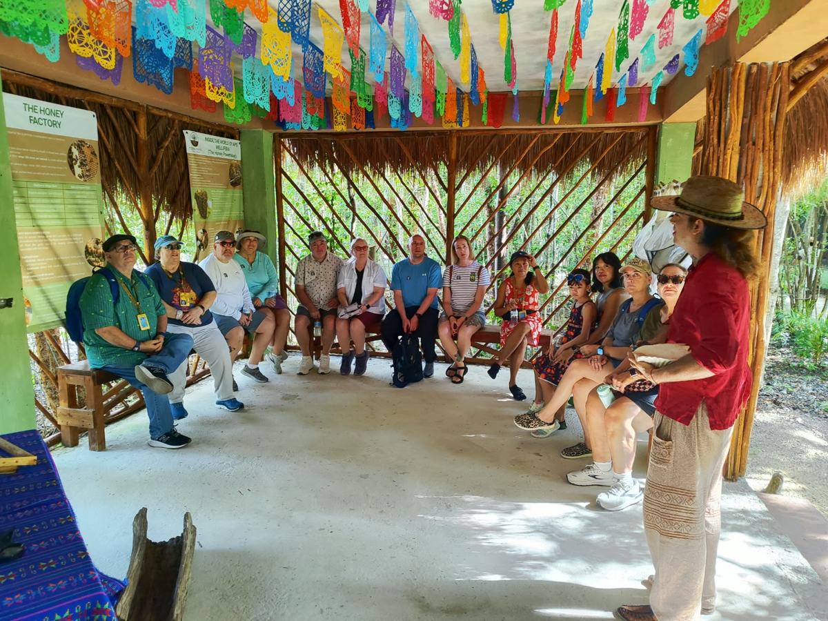Guests seated in a circle in the bee palapa, listening to a guide