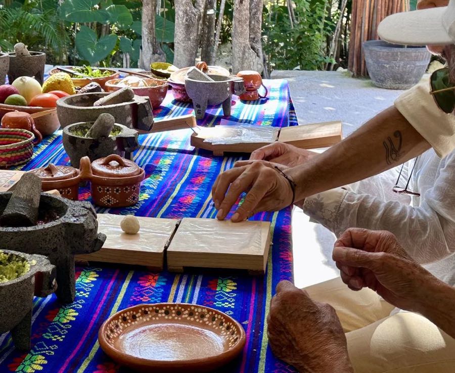 A table of stone molcajetes, clay bowls and fresh ingredients on a striped cloth