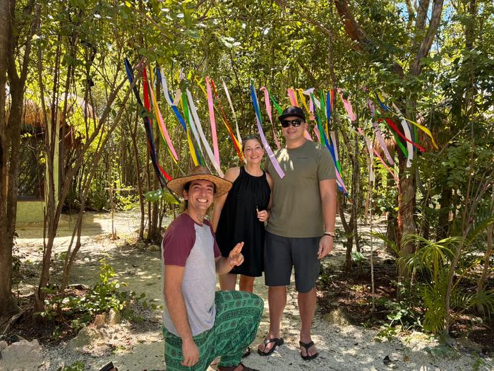 A laughing guide with two guests under coloured ribbons in the trees